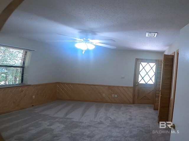 interior space featuring wood walls, ceiling fan, a textured ceiling, and carpet floors