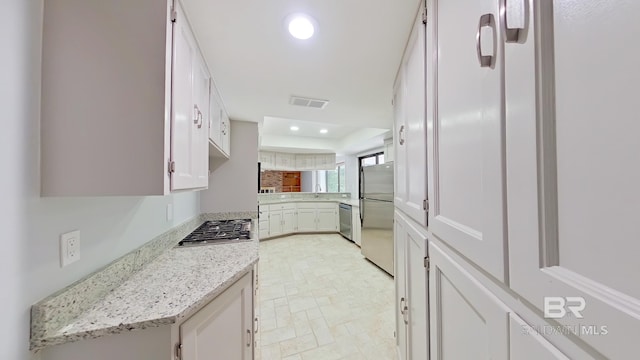 kitchen with appliances with stainless steel finishes, white cabinetry, light stone countertops, and sink