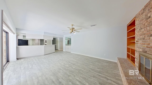 unfurnished living room featuring a fireplace, hardwood / wood-style flooring, built in features, and ceiling fan