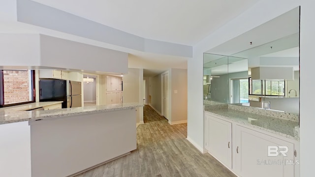 kitchen featuring kitchen peninsula, stainless steel fridge, white cabinets, light stone countertops, and light hardwood / wood-style floors