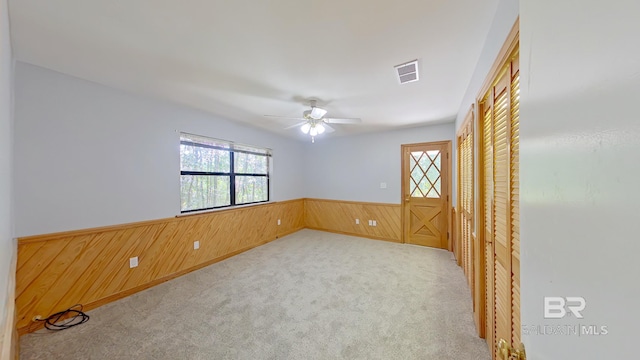 carpeted empty room featuring a healthy amount of sunlight, wooden walls, and ceiling fan