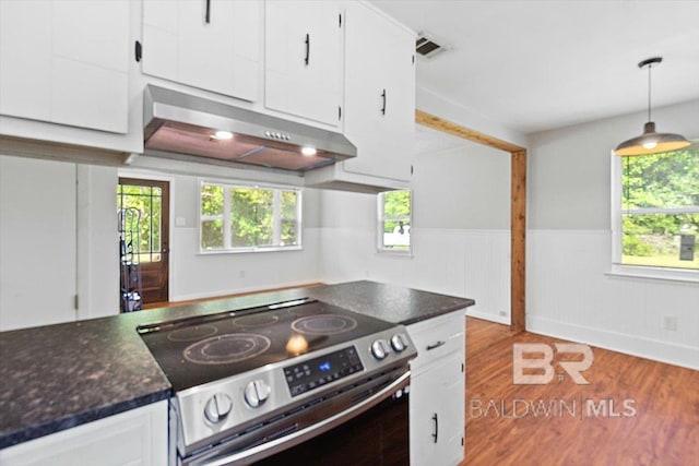 kitchen featuring dark countertops, stainless steel range with electric cooktop, a wainscoted wall, white cabinets, and under cabinet range hood