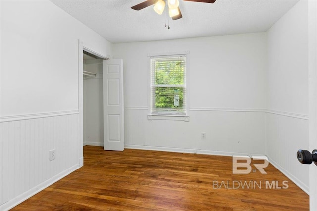 unfurnished bedroom with a ceiling fan, a textured ceiling, wood finished floors, baseboards, and a closet