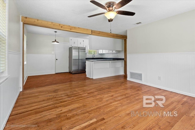 kitchen with freestanding refrigerator, dark countertops, visible vents, and wainscoting