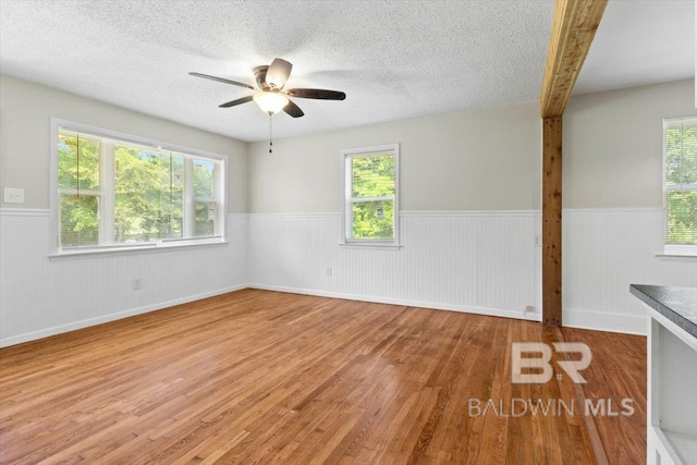 empty room featuring a ceiling fan, wainscoting, wood finished floors, and a healthy amount of sunlight