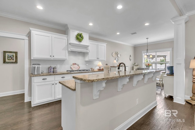 kitchen featuring light stone counters, dark wood finished floors, white cabinetry, stainless steel gas stovetop, and a kitchen bar