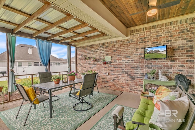 sunroom with a ceiling fan, outdoor dining area, and brick wall