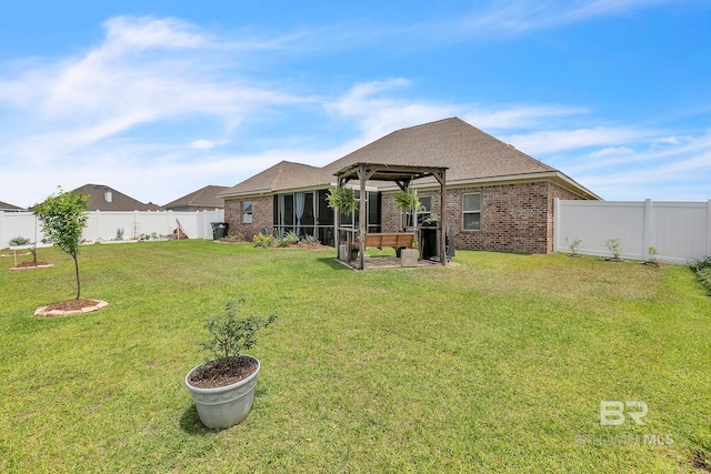 rear view of property featuring a lawn, brick siding, a fenced backyard, and a sunroom