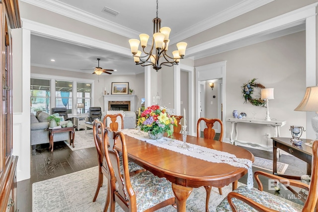 dining room with ornamental molding, ceiling fan with notable chandelier, a brick fireplace, and visible vents