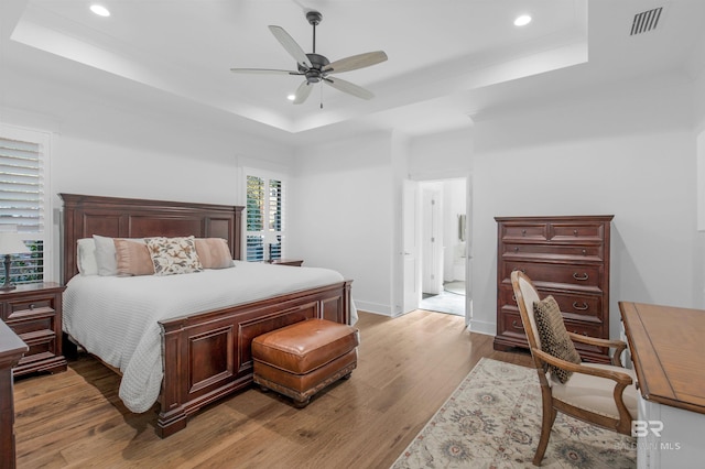 bedroom featuring light wood-type flooring, a tray ceiling, and ceiling fan