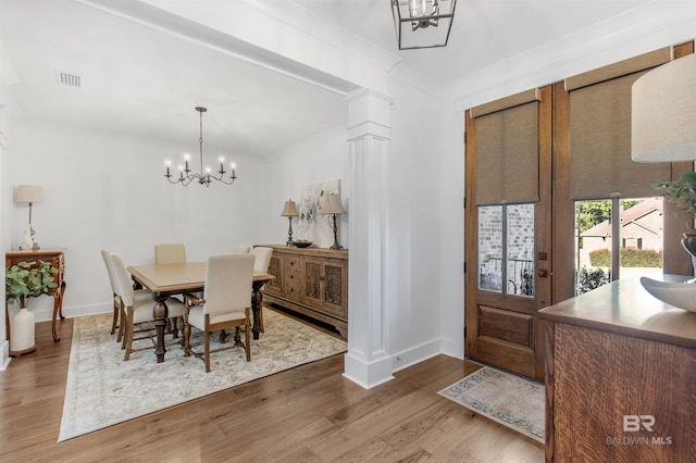 dining area with an inviting chandelier, hardwood / wood-style flooring, crown molding, and ornate columns