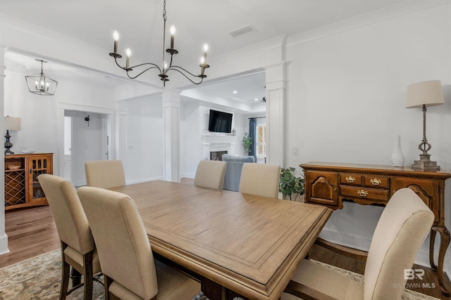 dining space with light wood-type flooring, crown molding, and decorative columns