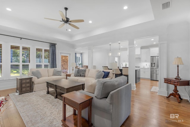 living room featuring light hardwood / wood-style floors, a tray ceiling, and ceiling fan