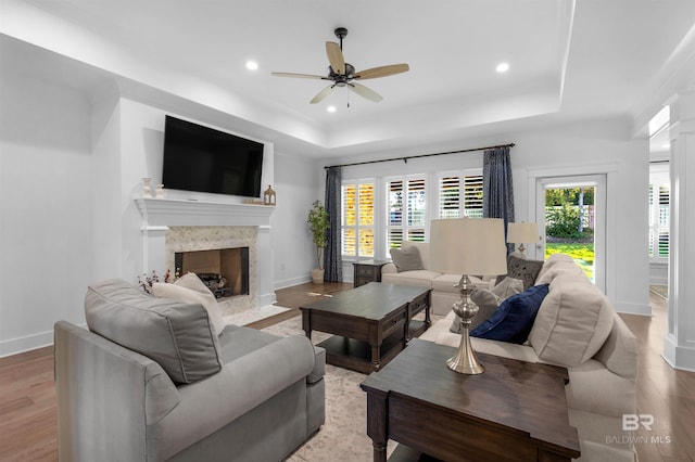 living room with light hardwood / wood-style floors, a raised ceiling, ceiling fan, decorative columns, and a premium fireplace