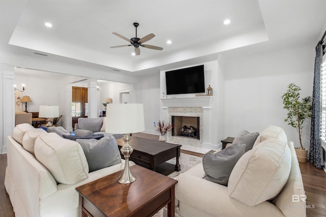 living room with a high end fireplace, ceiling fan, a raised ceiling, and hardwood / wood-style flooring