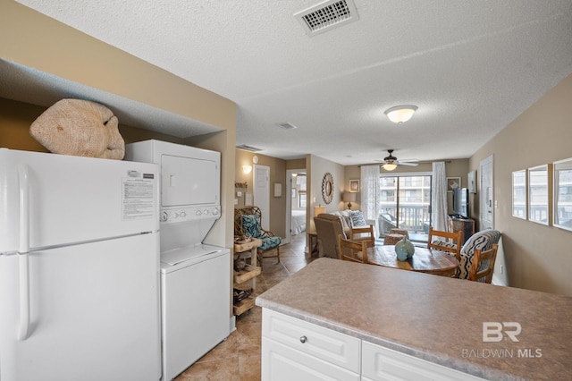 kitchen featuring white cabinetry, a textured ceiling, light tile patterned floors, white fridge, and stacked washer / dryer