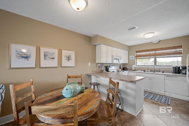 kitchen with white cabinetry, sink, a breakfast bar area, kitchen peninsula, and white appliances