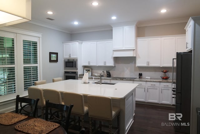 kitchen featuring crown molding, black appliances, dark hardwood / wood-style floors, decorative backsplash, and a kitchen island with sink