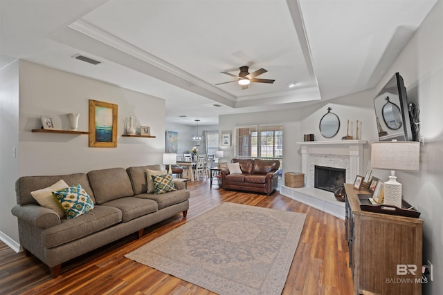 living room featuring wood finished floors, visible vents, a fireplace, crown molding, and a raised ceiling