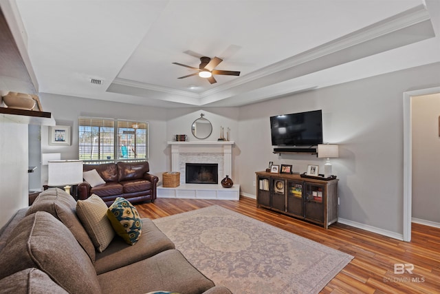 living area featuring visible vents, a tray ceiling, wood finished floors, crown molding, and a tile fireplace