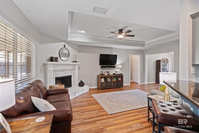 living room featuring light wood finished floors, a fireplace, a raised ceiling, and ornamental molding