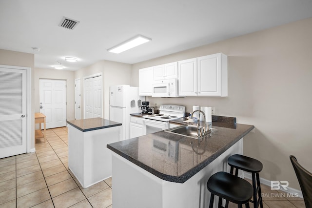 kitchen with a peninsula, white appliances, a breakfast bar, a sink, and visible vents