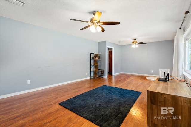 living area with visible vents, a ceiling fan, baseboards, and wood finished floors