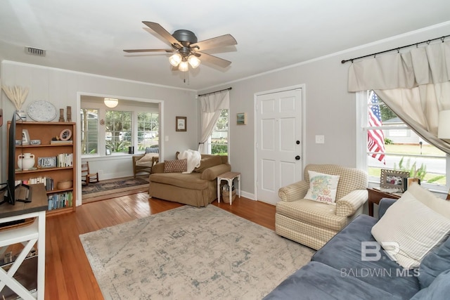 living area featuring visible vents, wood finished floors, a ceiling fan, and ornamental molding