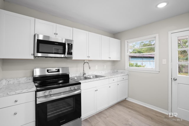 kitchen with sink, white cabinetry, light stone counters, light wood-type flooring, and stainless steel appliances