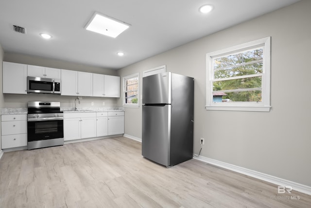 kitchen featuring stainless steel appliances, sink, white cabinetry, a healthy amount of sunlight, and light hardwood / wood-style floors