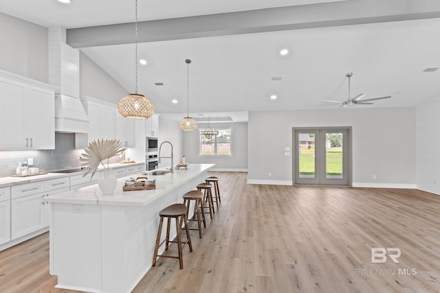 11341 Tall Timber Ln, Elberta, AL 36530 - kitchen featuring a large island with sink, white cabinets, light wood finished floors, decorative backsplash, and stainless steel microwave