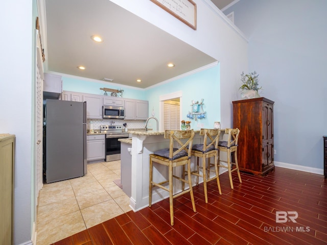 kitchen with gray cabinetry, light wood-type flooring, stainless steel appliances, a breakfast bar area, and ornamental molding