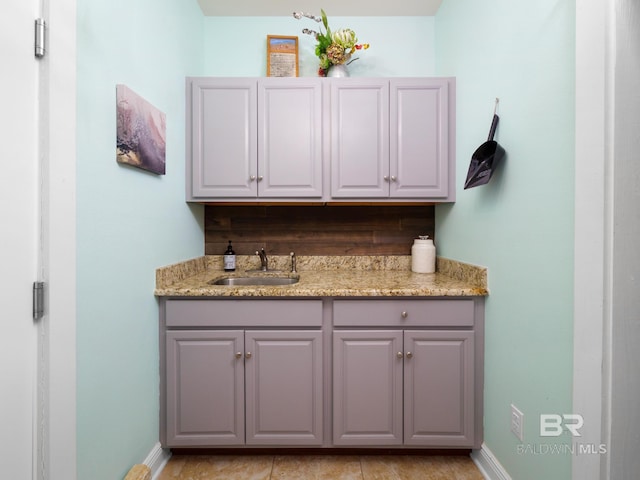 bar with gray cabinets, sink, and light stone countertops