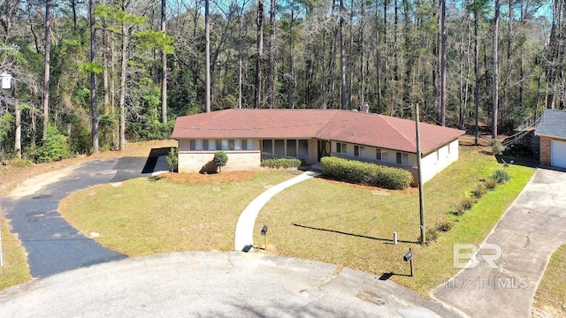 view of front of house with aphalt driveway, a front yard, and a view of trees