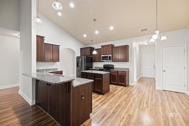 kitchen featuring appliances with stainless steel finishes, pendant lighting, a breakfast bar area, light stone counters, and kitchen peninsula