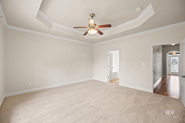 empty room featuring a raised ceiling, crown molding, ceiling fan, and dark carpet