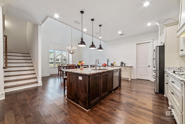 kitchen featuring pendant lighting, appliances with stainless steel finishes, sink, light stone countertops, and a center island with sink