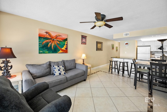 living area with visible vents, a textured ceiling, light tile patterned floors, baseboards, and ceiling fan