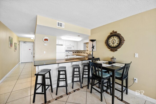 kitchen with light tile patterned floors, visible vents, white appliances, and a peninsula