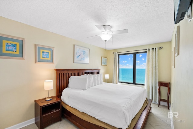 bedroom with baseboards, a water view, light tile patterned floors, a textured ceiling, and a ceiling fan