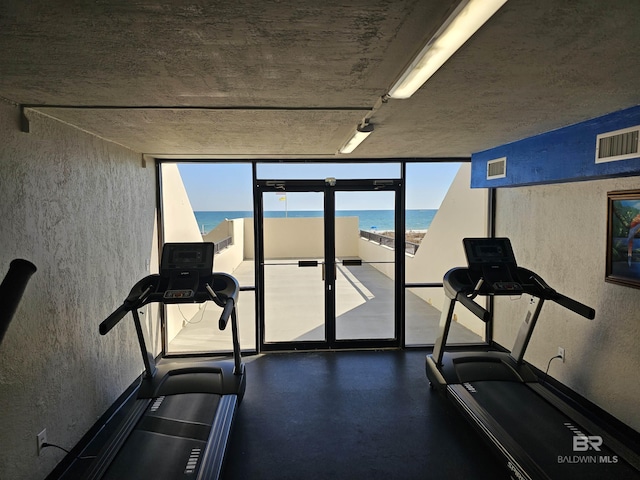 exercise room featuring visible vents, a water view, and floor to ceiling windows