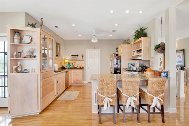 kitchen featuring kitchen peninsula, light brown cabinets, a kitchen bar, light hardwood / wood-style floors, and tasteful backsplash