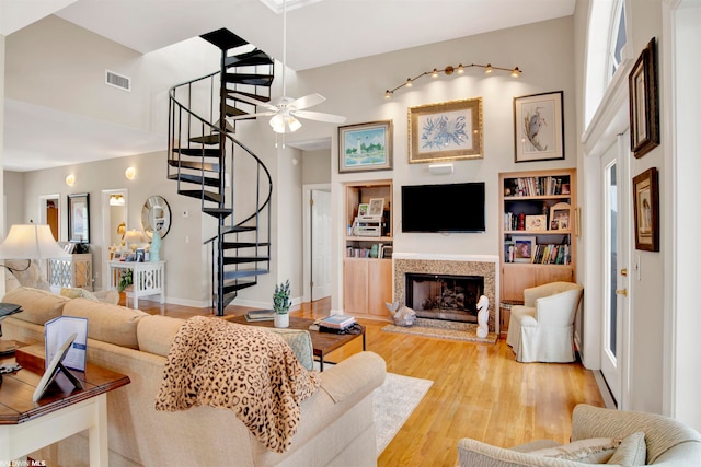 living room featuring a high end fireplace, ceiling fan, built in features, a wealth of natural light, and light wood-type flooring