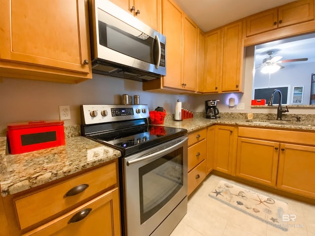 kitchen with stainless steel appliances, light stone countertops, light tile patterned floors, ceiling fan, and sink