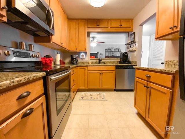 kitchen featuring light stone counters, light tile patterned floors, appliances with stainless steel finishes, ceiling fan, and sink