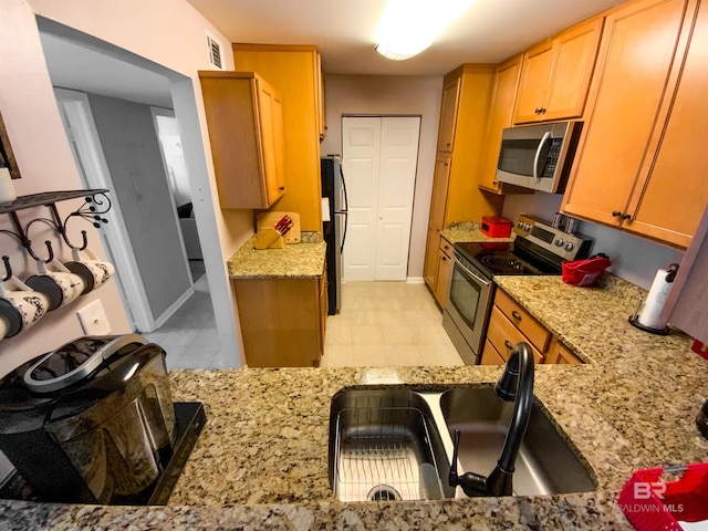 kitchen with appliances with stainless steel finishes, light stone counters, and sink