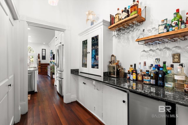 bar featuring white cabinets, dark wood-type flooring, dark stone countertops, and stainless steel refrigerator