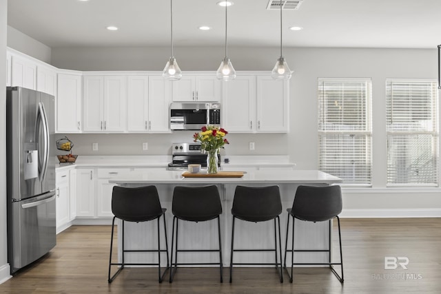 kitchen with decorative light fixtures, white cabinets, a center island, stainless steel appliances, and dark wood-type flooring