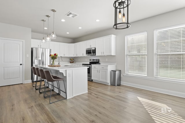 kitchen with sink, appliances with stainless steel finishes, an island with sink, white cabinets, and decorative light fixtures