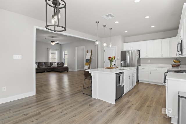 kitchen featuring sink, appliances with stainless steel finishes, hanging light fixtures, white cabinets, and a center island with sink